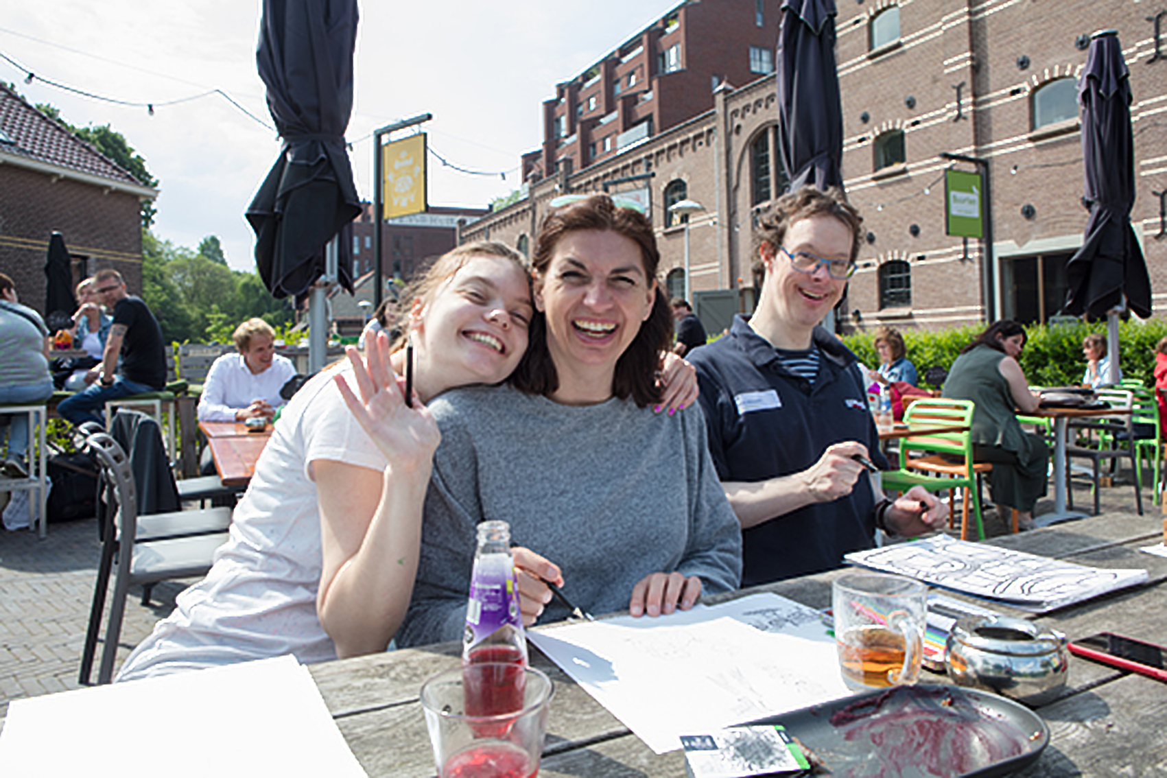 Derk samen met twee lachende dames tekenen buiten aan een picknicktafel.