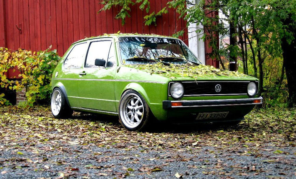 Foto van een groene Volkswagen Golf bedekt met bladeren in herfstlandschap.