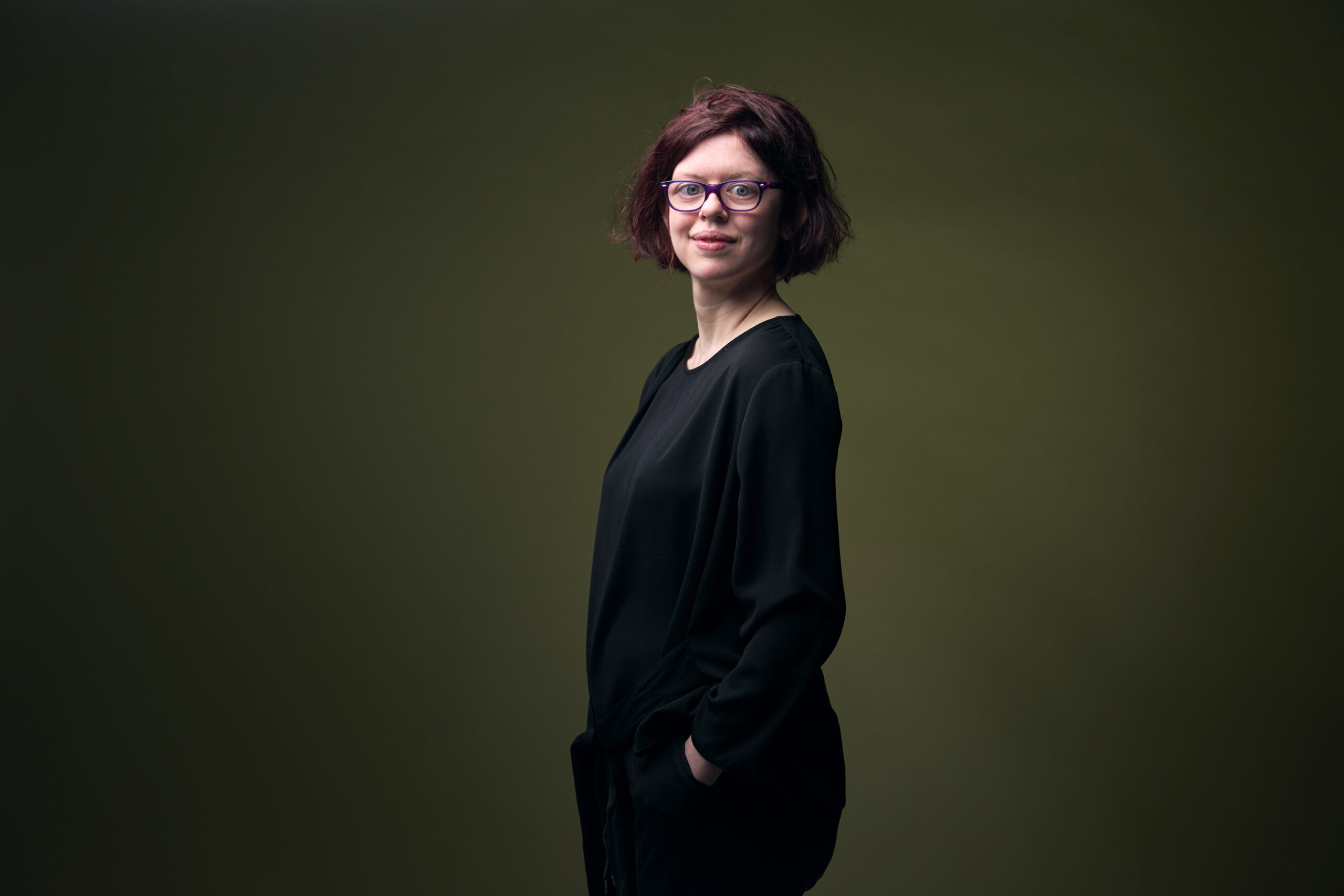 Britt-Marie, een meisje met een verstandelijke beperking, die naar links gedraaid is, haar handen in haar zakken heeft en naar je glimlacht