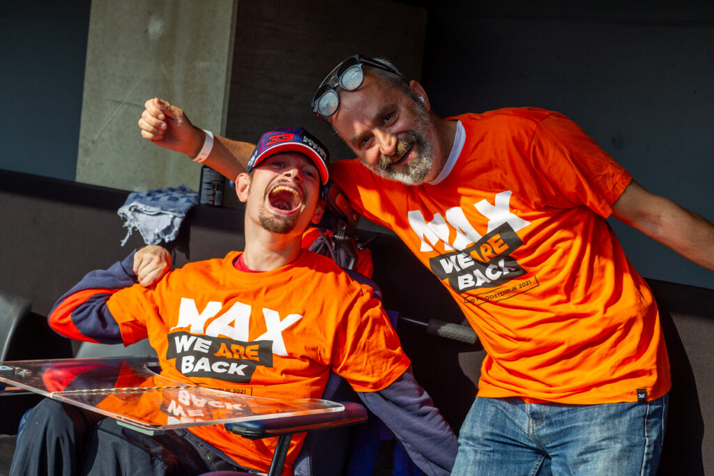 Een jongen met een beperking en een man staan samen te juichen voor Max Verstappen bij de Dutch Grand Prix