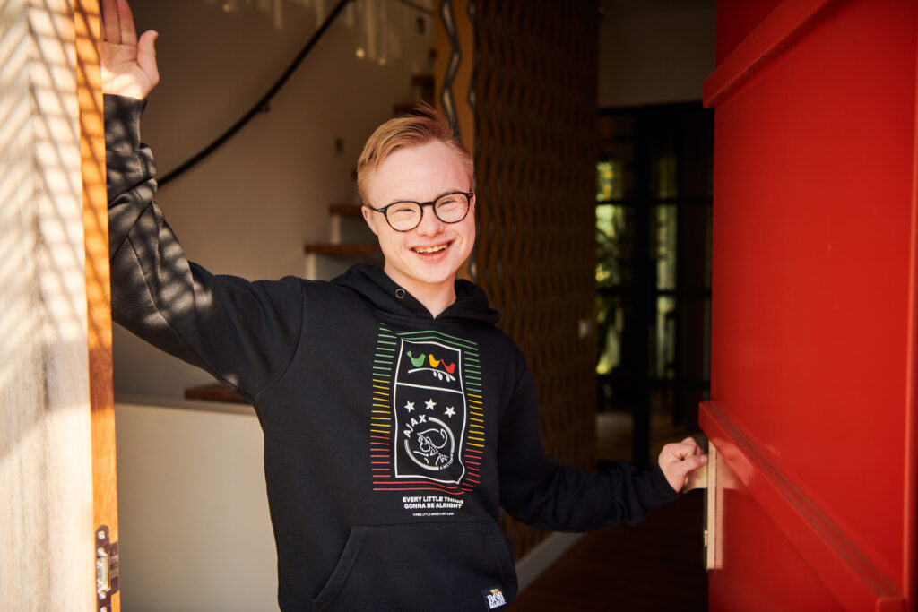 Gijs, een jongen met het Syndroom van Down, die in een deuropening staat en lacht