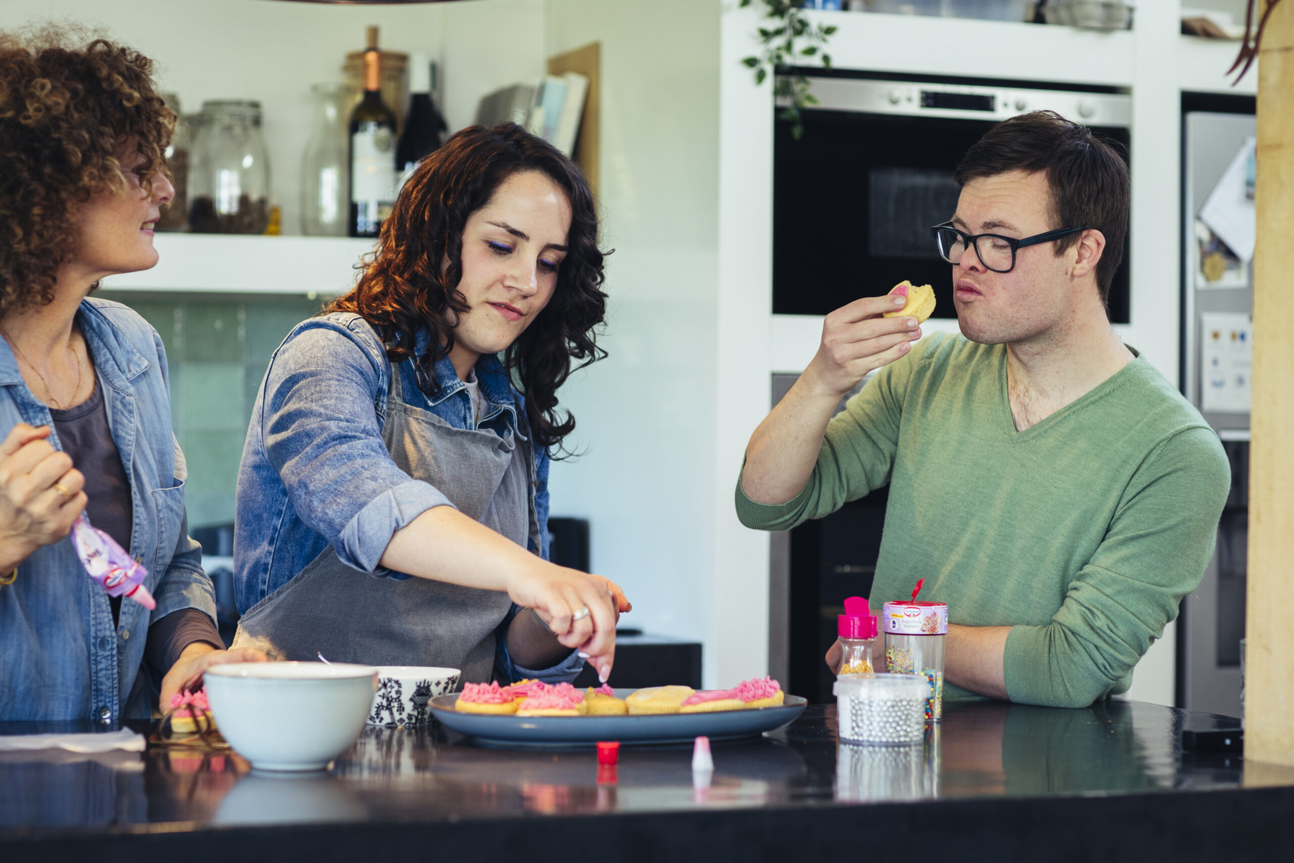 Een jongen met het syndroom van Down staat samen met twee vrouwen cupcakes te bakken en te proeven