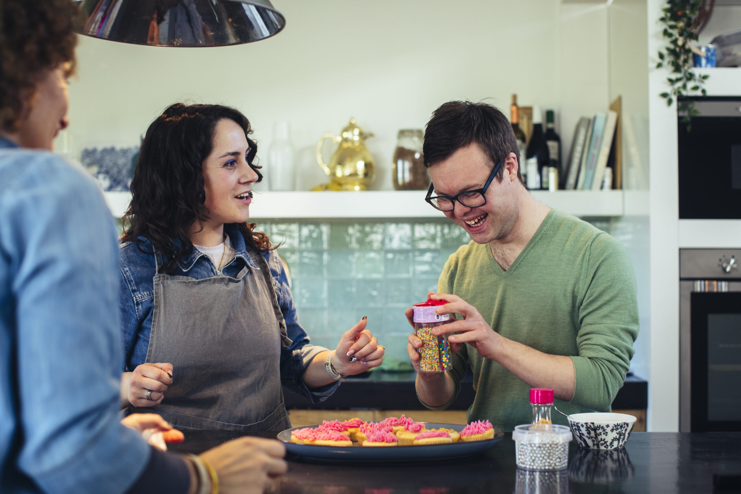 Een jongen met het syndroom van Down staat samen met twee vrouwen cupcakes te bakken
