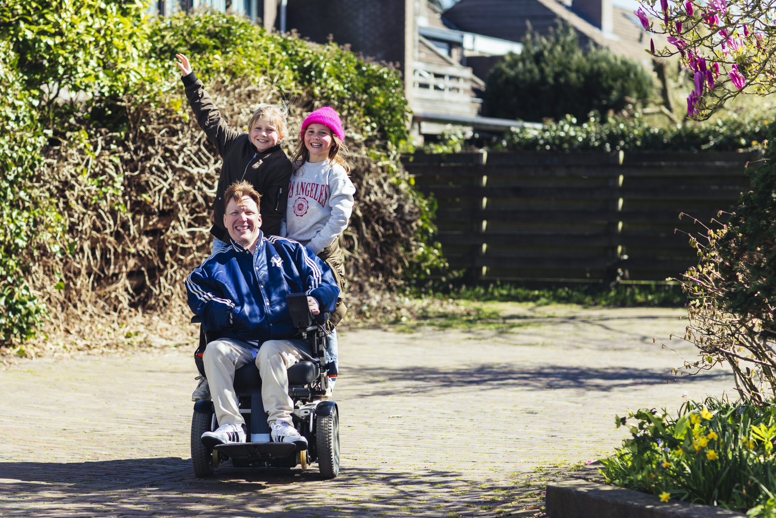 Twee meisjes zitten achterop bij een man die in een rolstoel zit, ze lachen