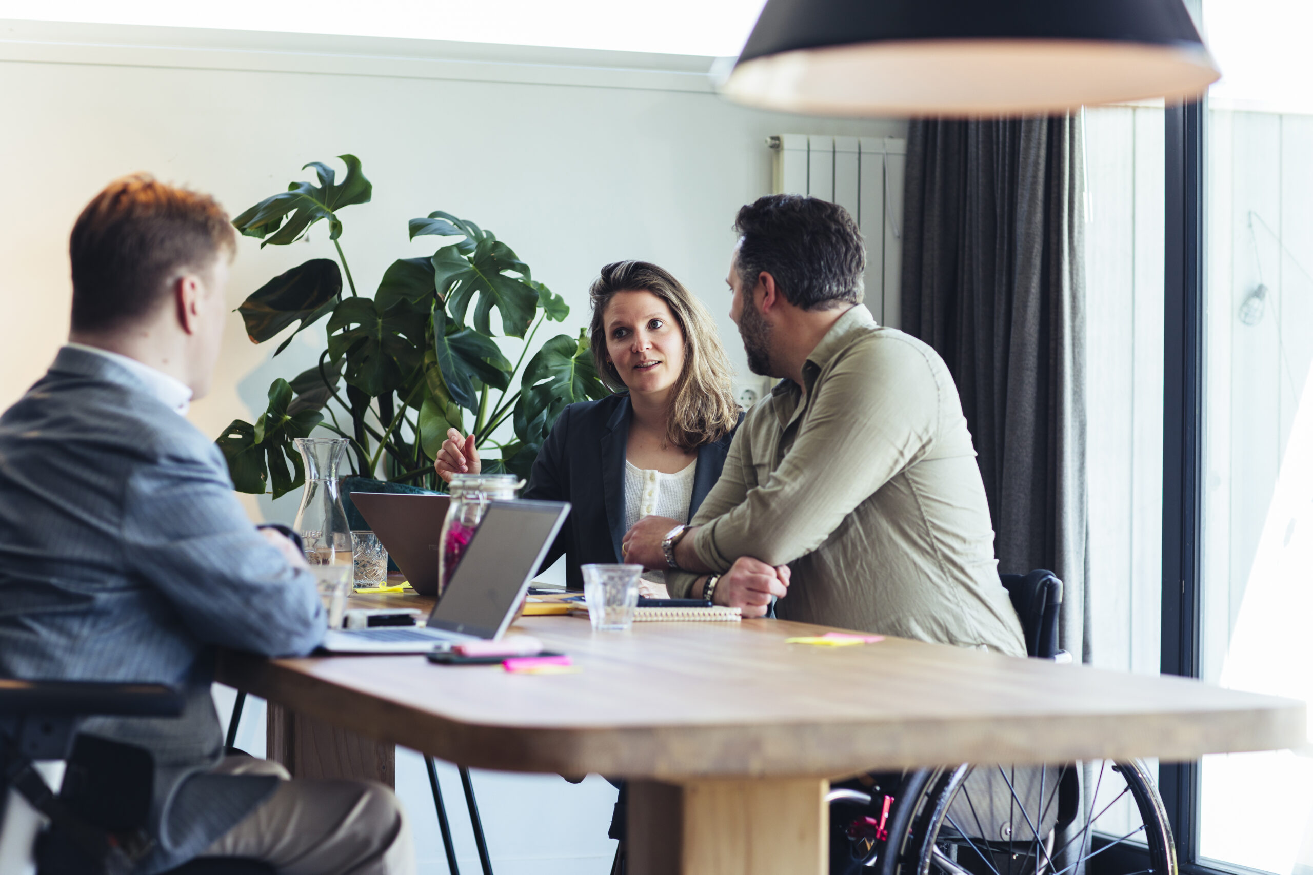 Drie mensen zijn met elkaar aan het overleggen, ze hebben laptops voor zich en notitiepapieren