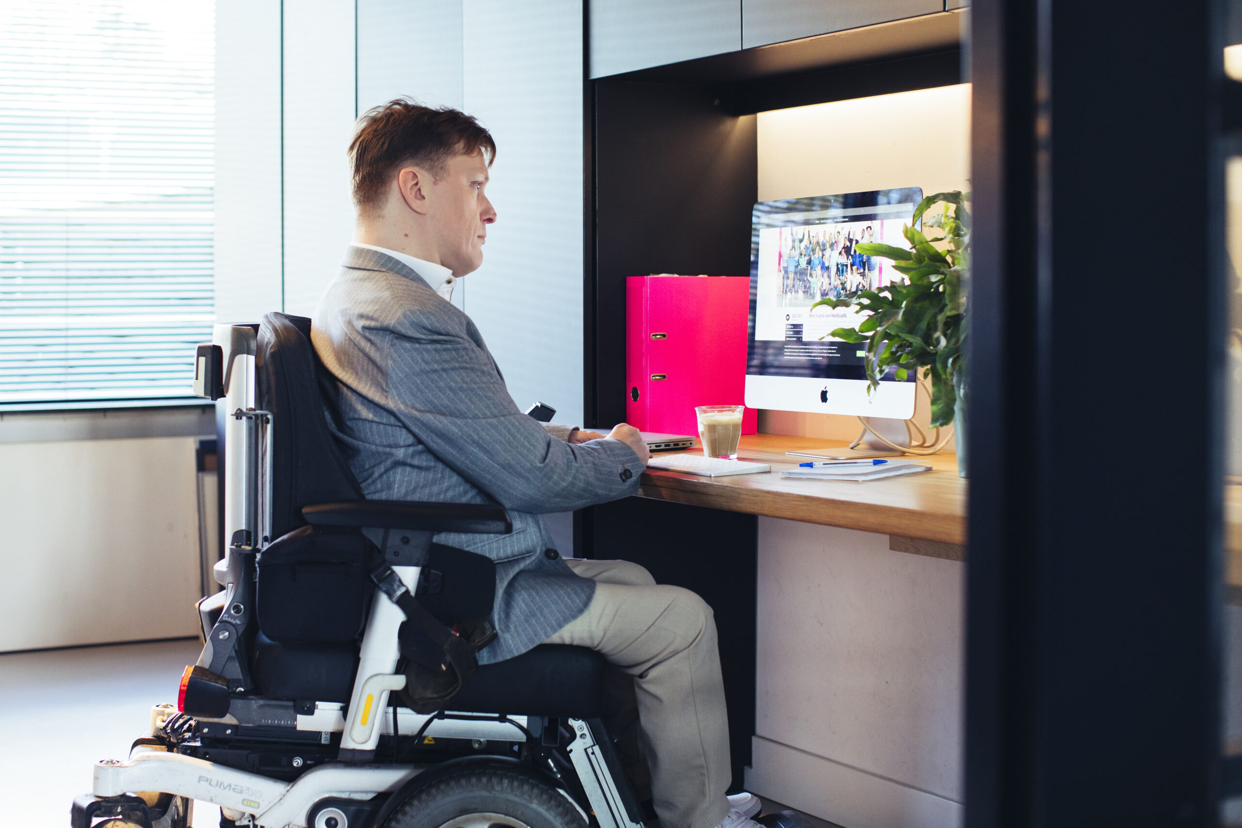 Frank, een man met een fysieke beperking, zit in zijn rolstoel achter een bureau en is aan het werk