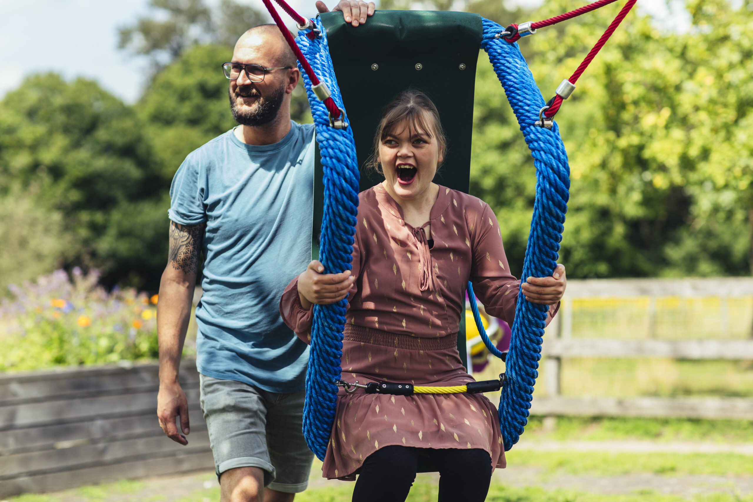 Een meisje met een verstandelijke beperking is aan het schommelen en wordt geduwd door een man, het meisje lacht
