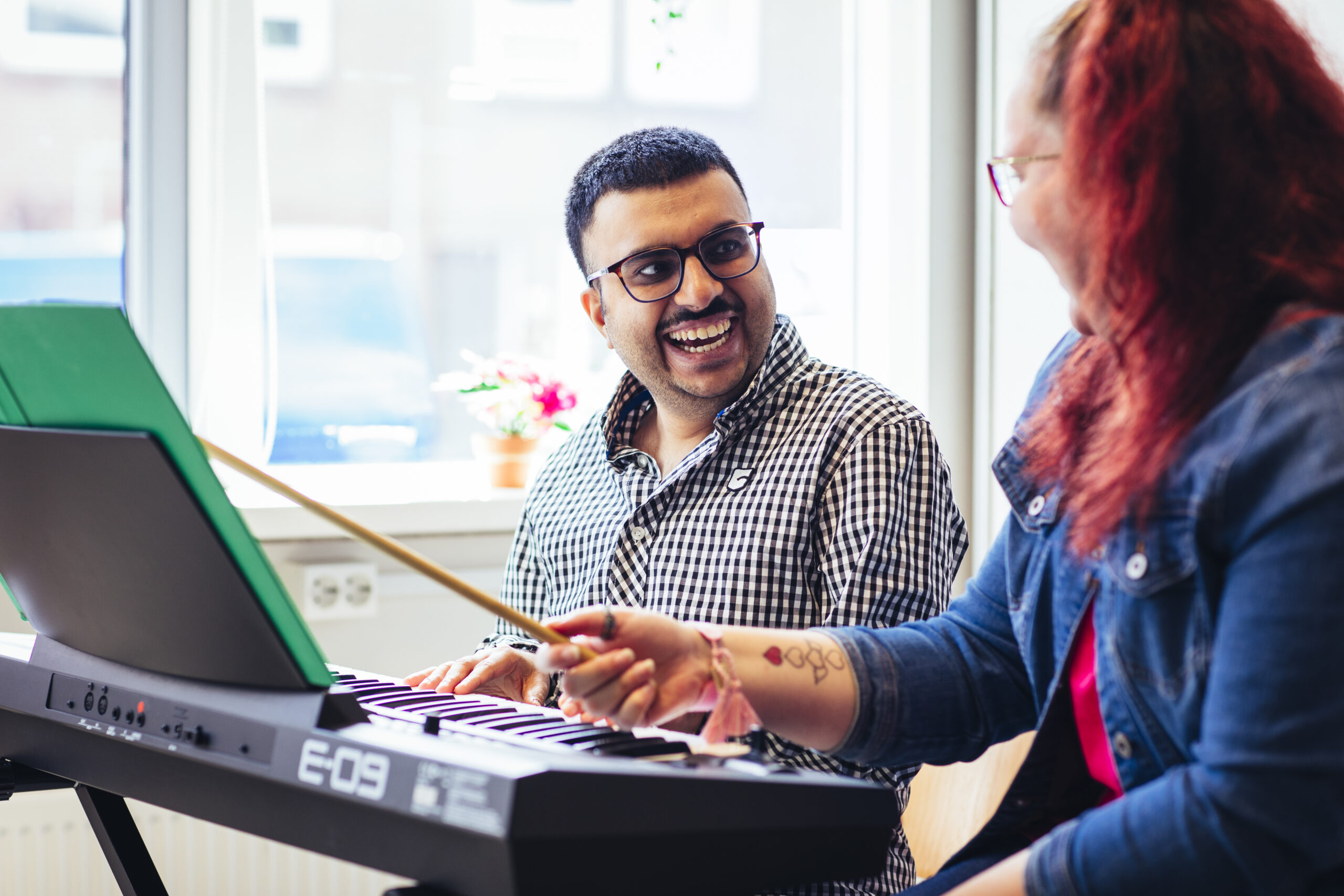 Dhiraj zit achter een keyboard en krijgt les van een vrouw