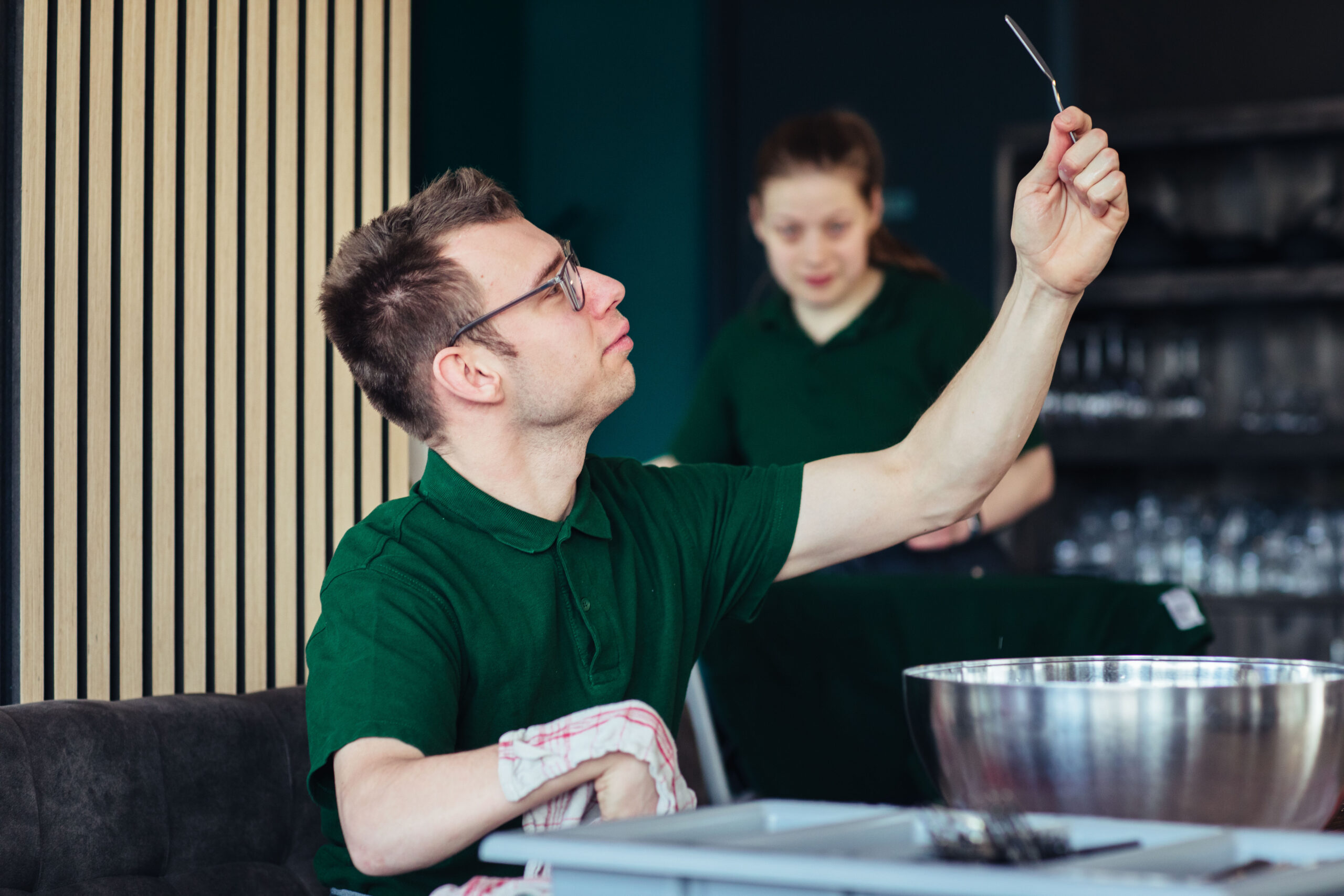 Een jongen met een verstandelijke beperking die werkzaam is bij Lunchroom Beetje Bijzonder. Hij droogt het bestek en controleert of dit goed is gelukt