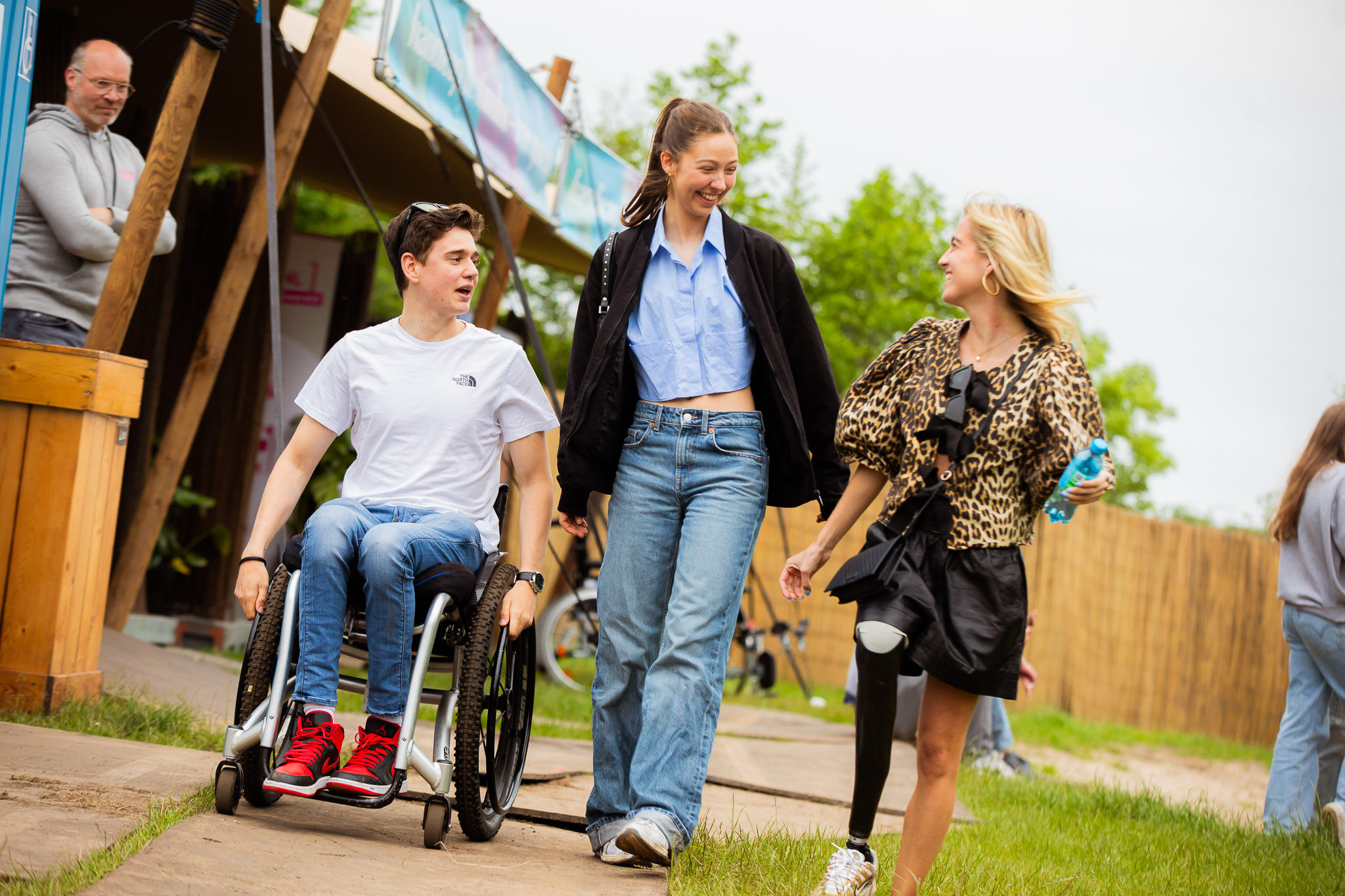 Twee meisjes, waarvan één een kunstbeen heeft, en een jongen in rolstoel bewegen zich over het festivalterrein en lachen naar elkaar