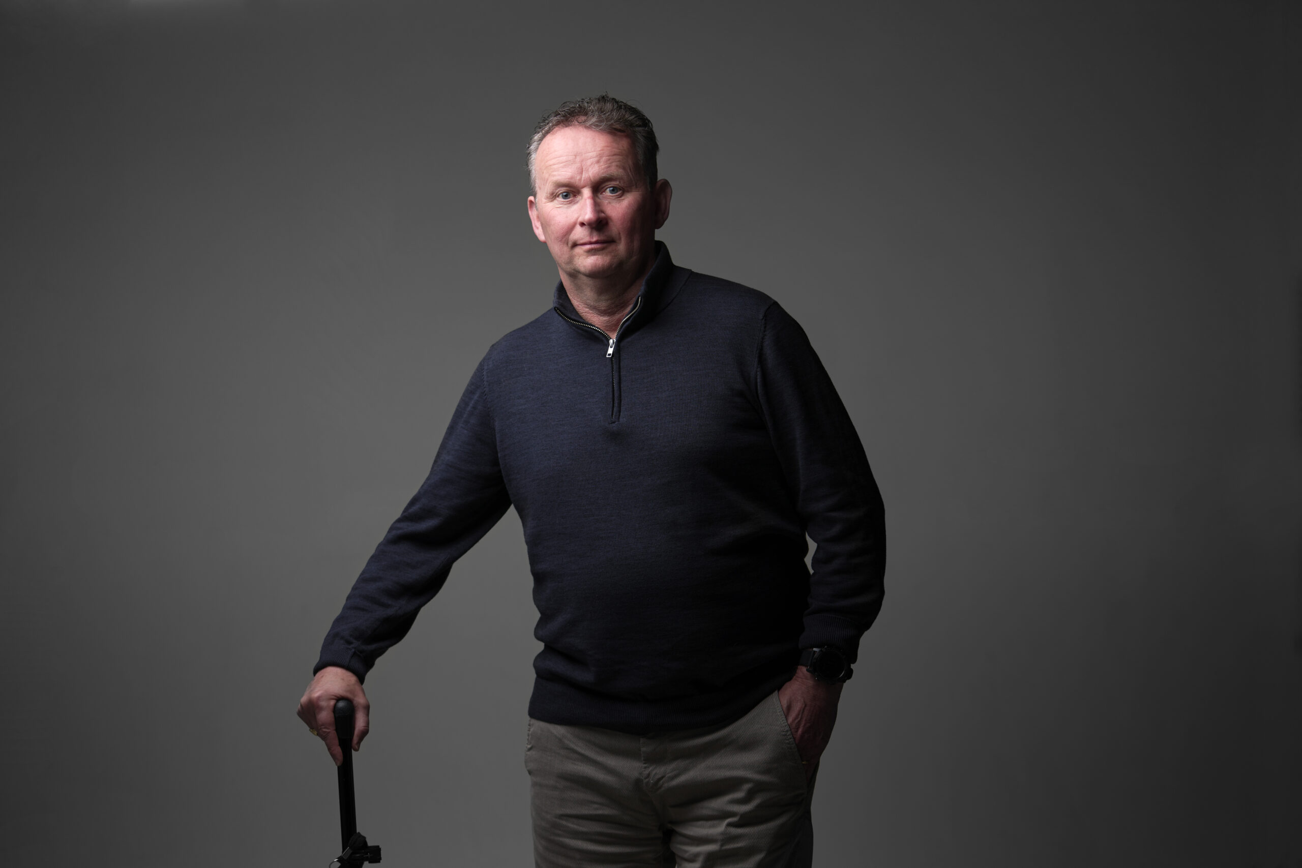 Wim, een man met een fysieke beperking, die je aankijkt en leunt op zijn wandelstok