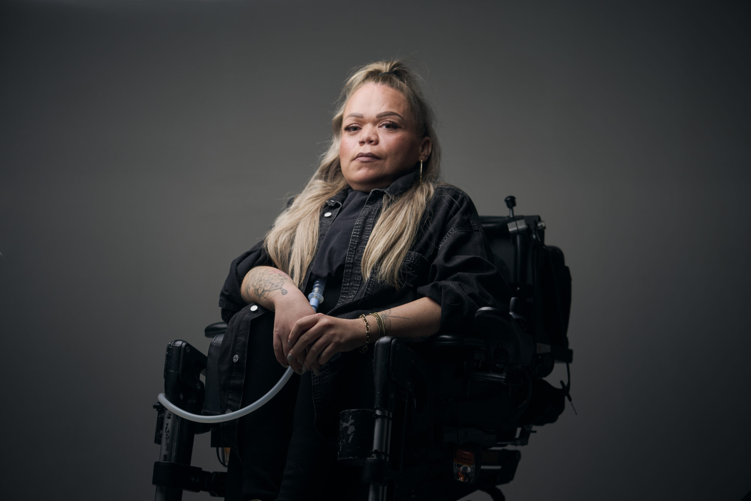 Roos, een vrouw met een fysieke beperking, die in een rolstoel zit en je zelfverzekerd aankijkt