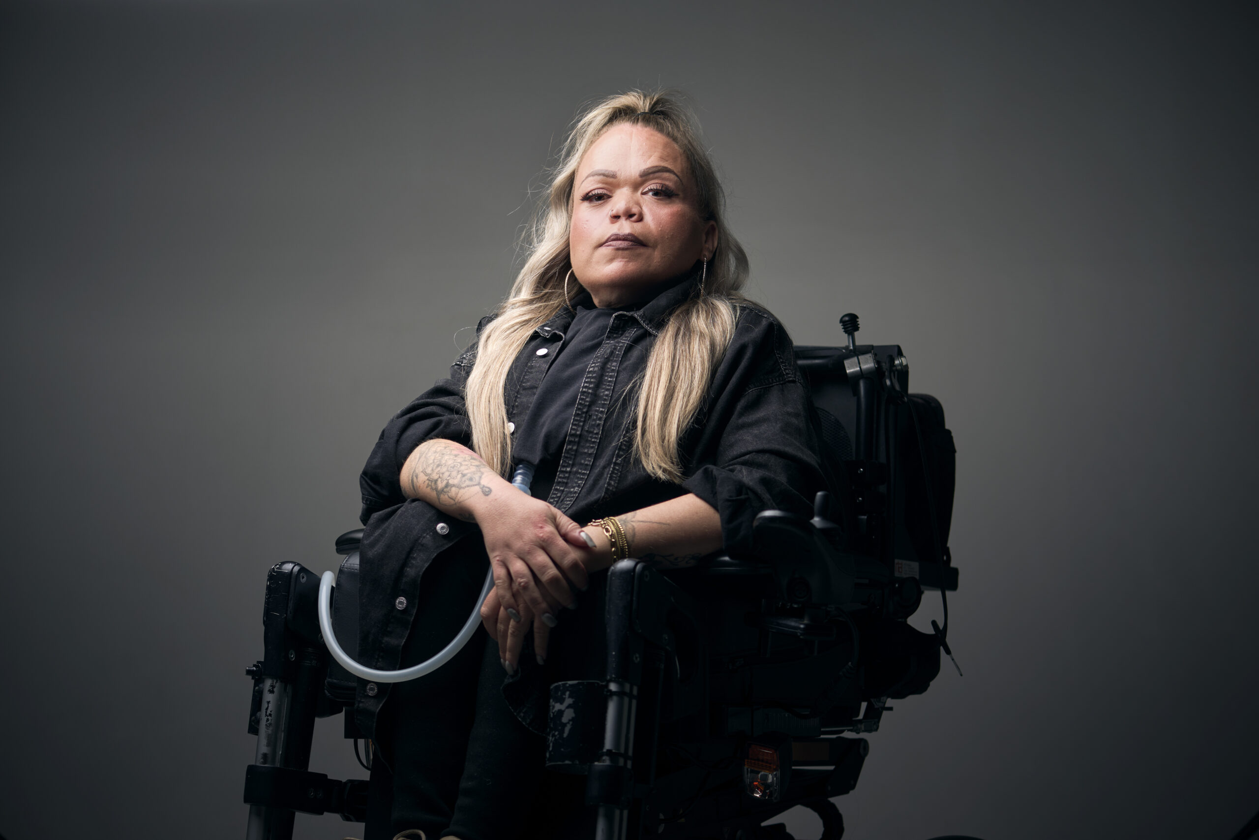 Roos, een vrouw met een fysieke beperking, die in een rolstoel zit en je zelfverzekerd aankijkt