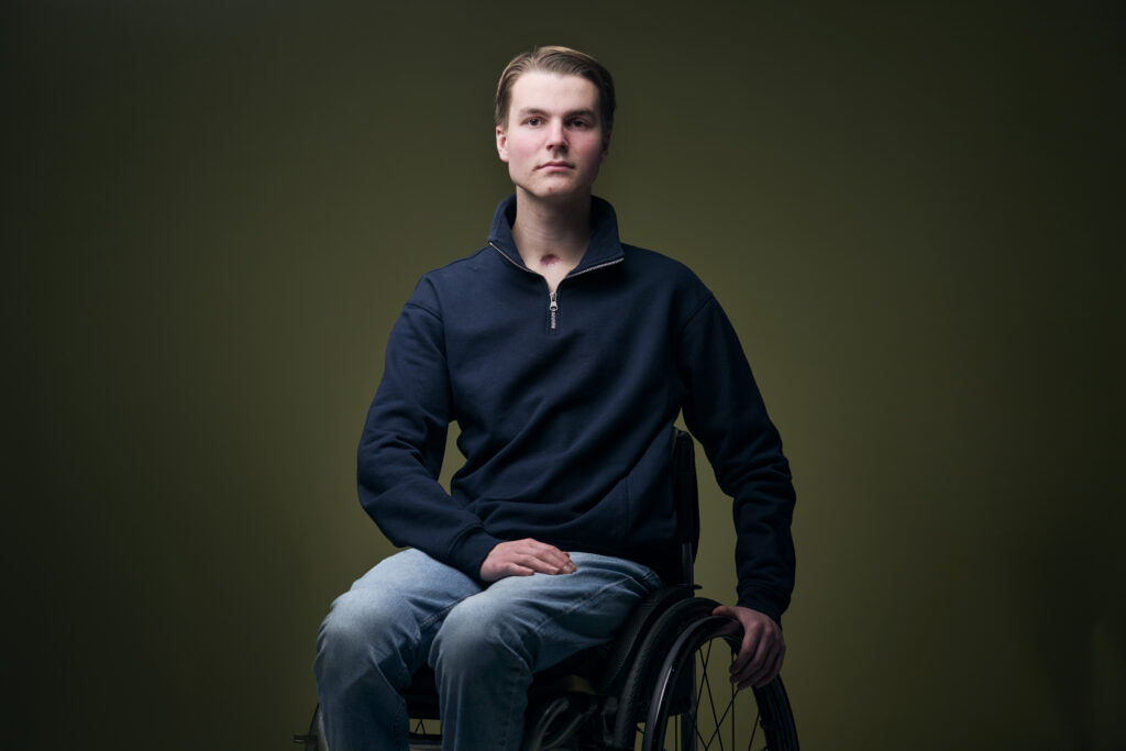Cees, een jongen met een fysieke beperking, die in een rolstoel zit en je recht aankijkt