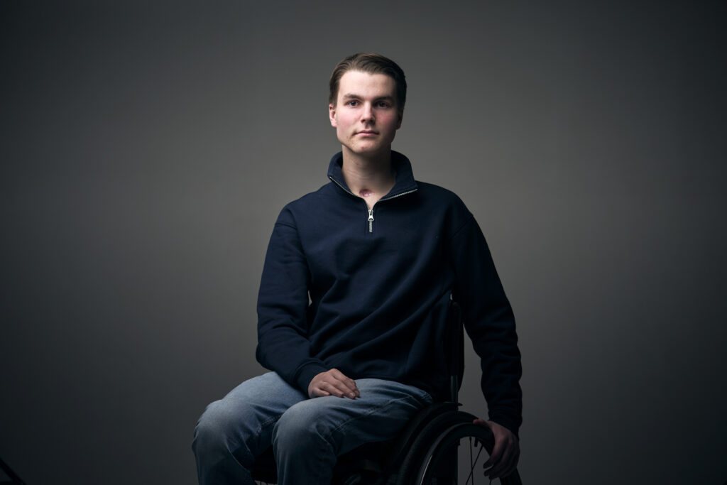 Cees, een jongen met een fysieke beperking, die in een rolstoel zit en je recht aankijkt