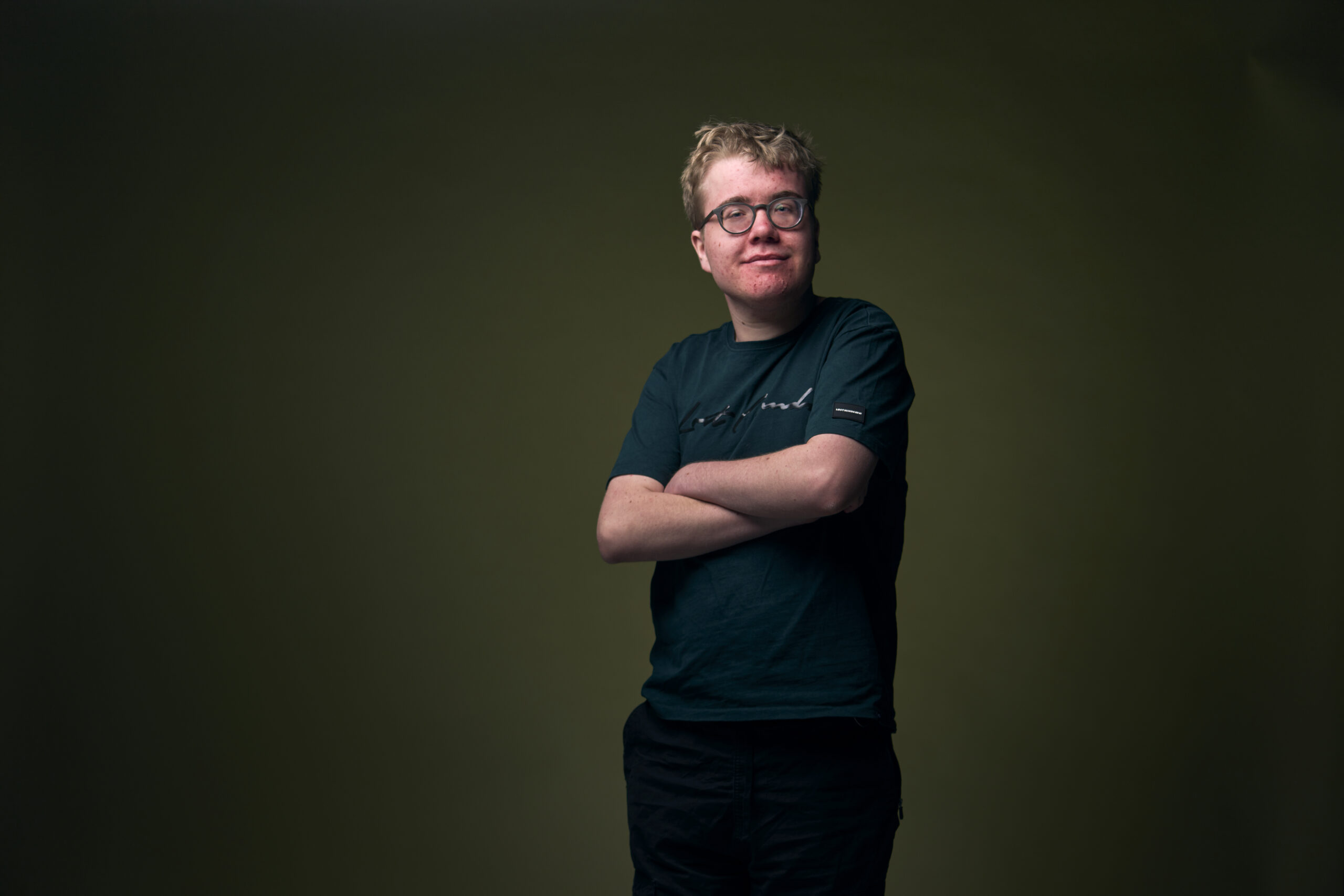 Tijn, een jongen met een verstandelijke beperking, die zijn armen over elkaar heen houdt en naar je glimlacht