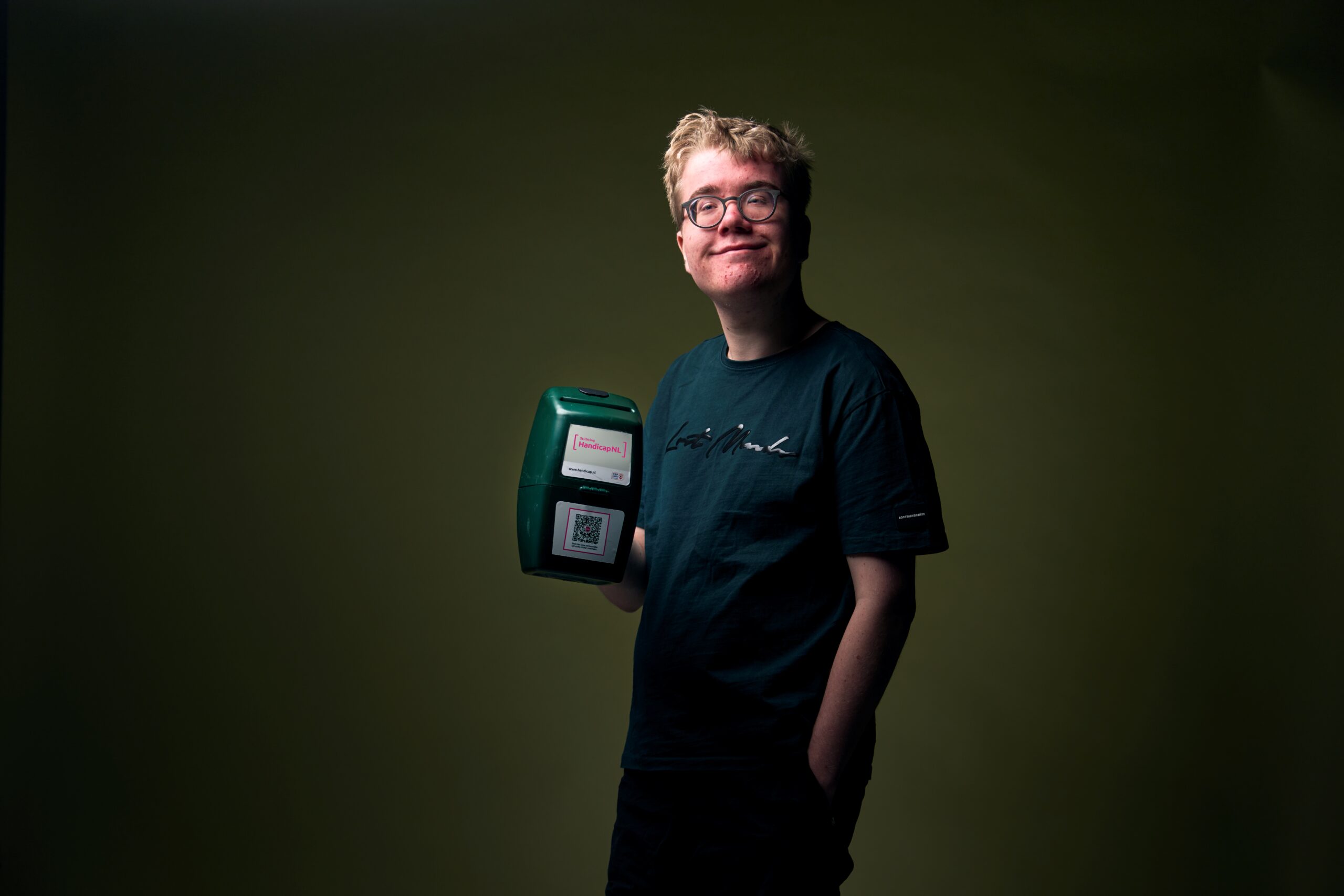 Tijn, een jongen met een verstandelijke beperking, die een collectebus vasthoud en glimlacht
