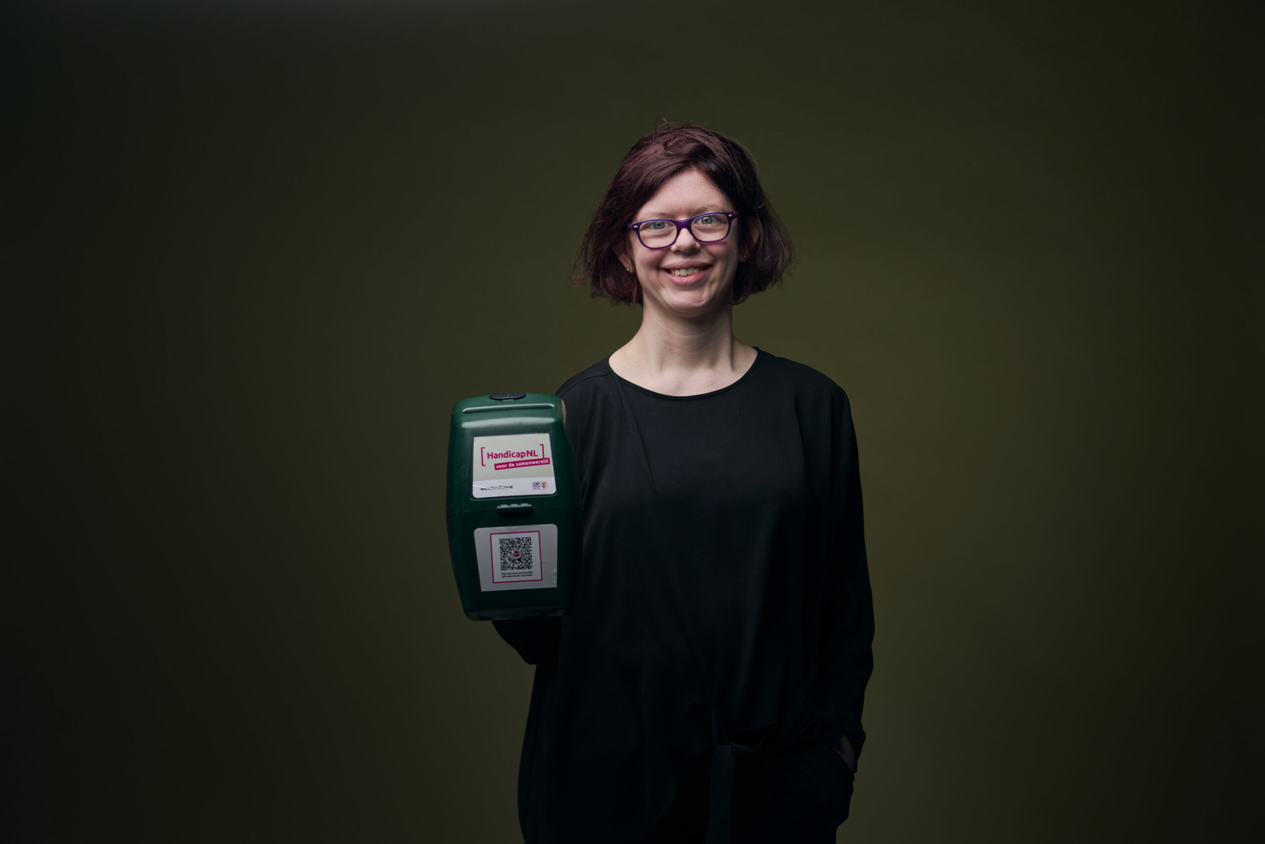 Britt-Marie, een meisje met een verstandelijke beperking, die je lachend aankijkt en een collectebus vasthoudt.