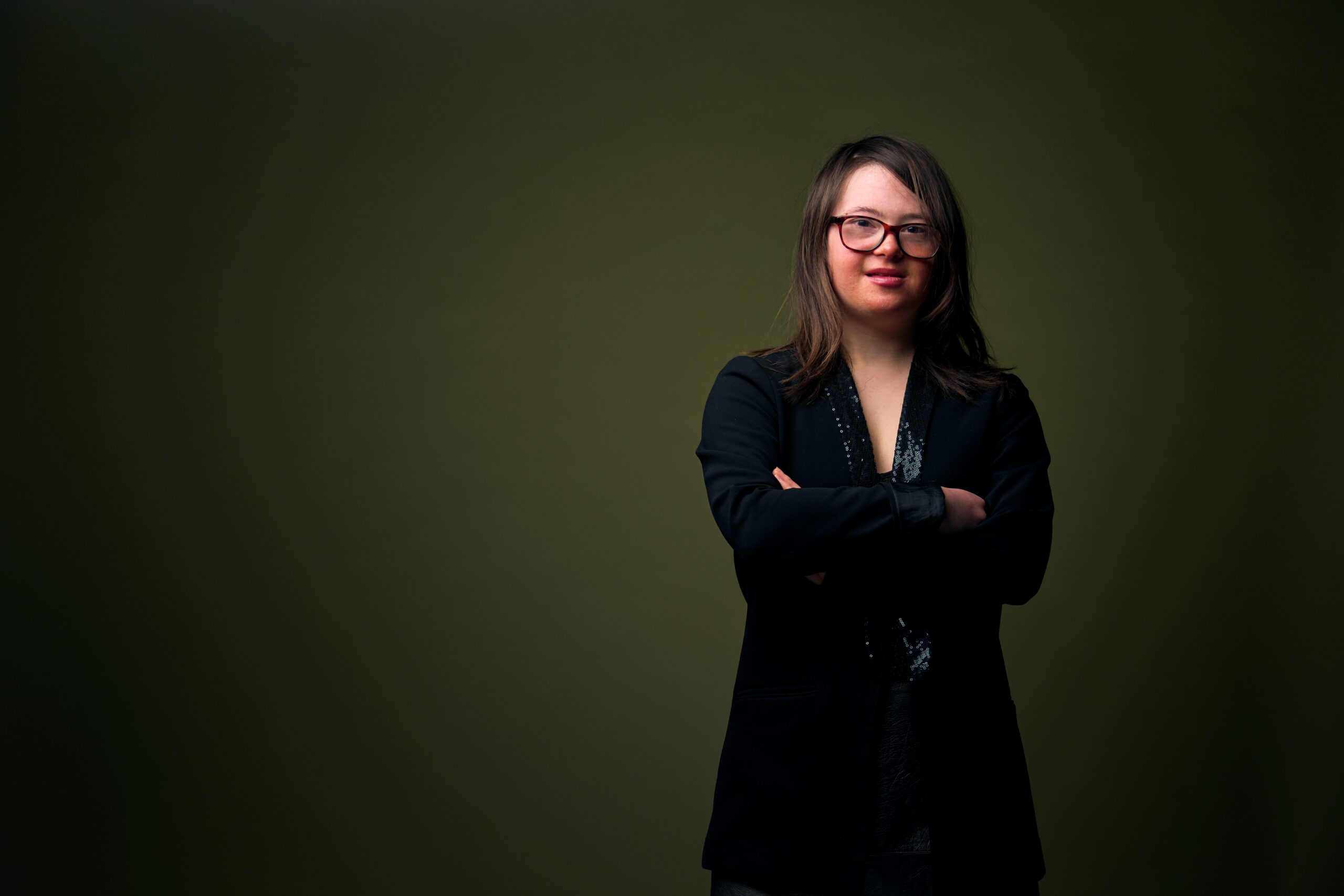 Tess, een meisje met het Syndroom van Down, die met haar armen over elkaar heen staat