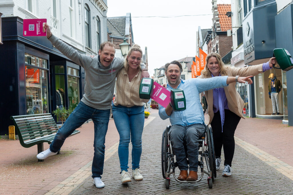 Het team van HandicapNL staat met collectebussen in een stad, ze omhelzen elkaar en zijn blij