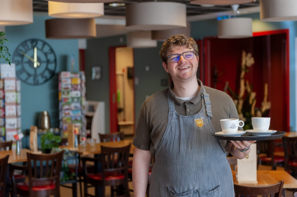 Een jongen met een verstandelijke beperking, die werkzaam is bij Prins Heerlijk serveert koffie