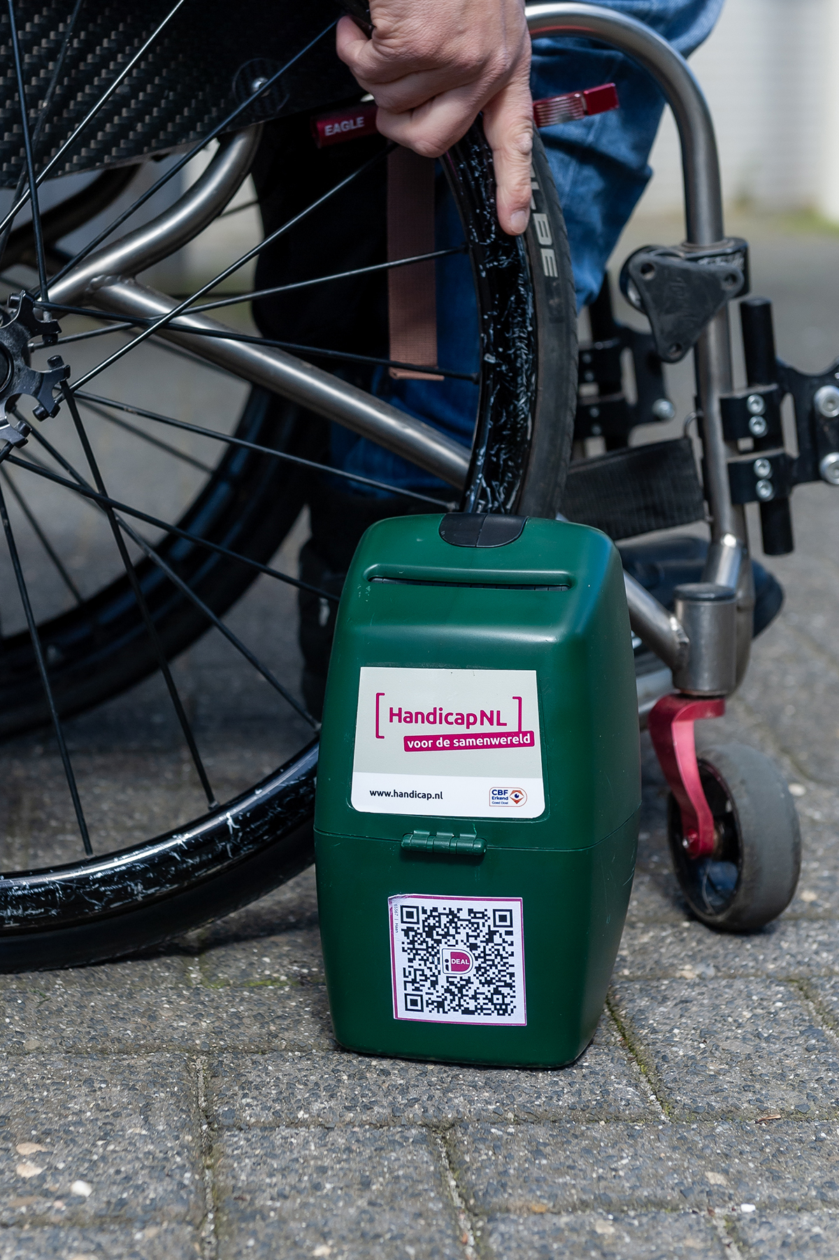 Een collectebus van HandicapNL staat op de stoep naast een rolstoel