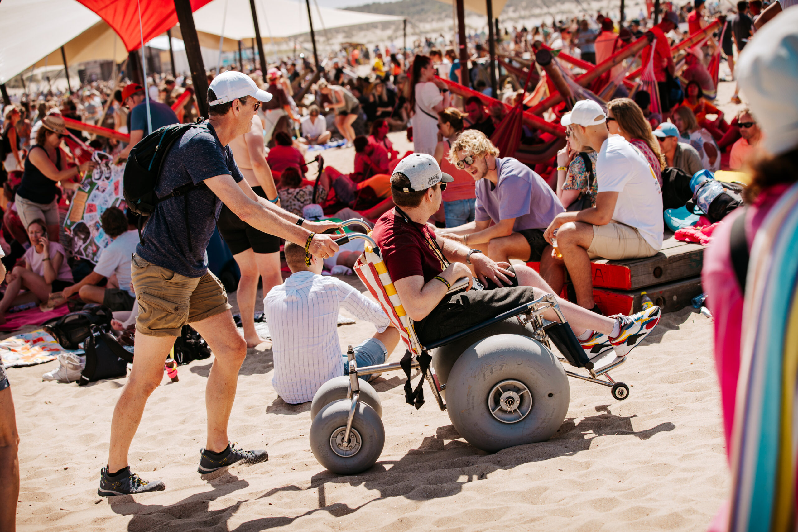 Een man met een fysieke beperking wordt vooruit geduwd in een strandrolstoel.