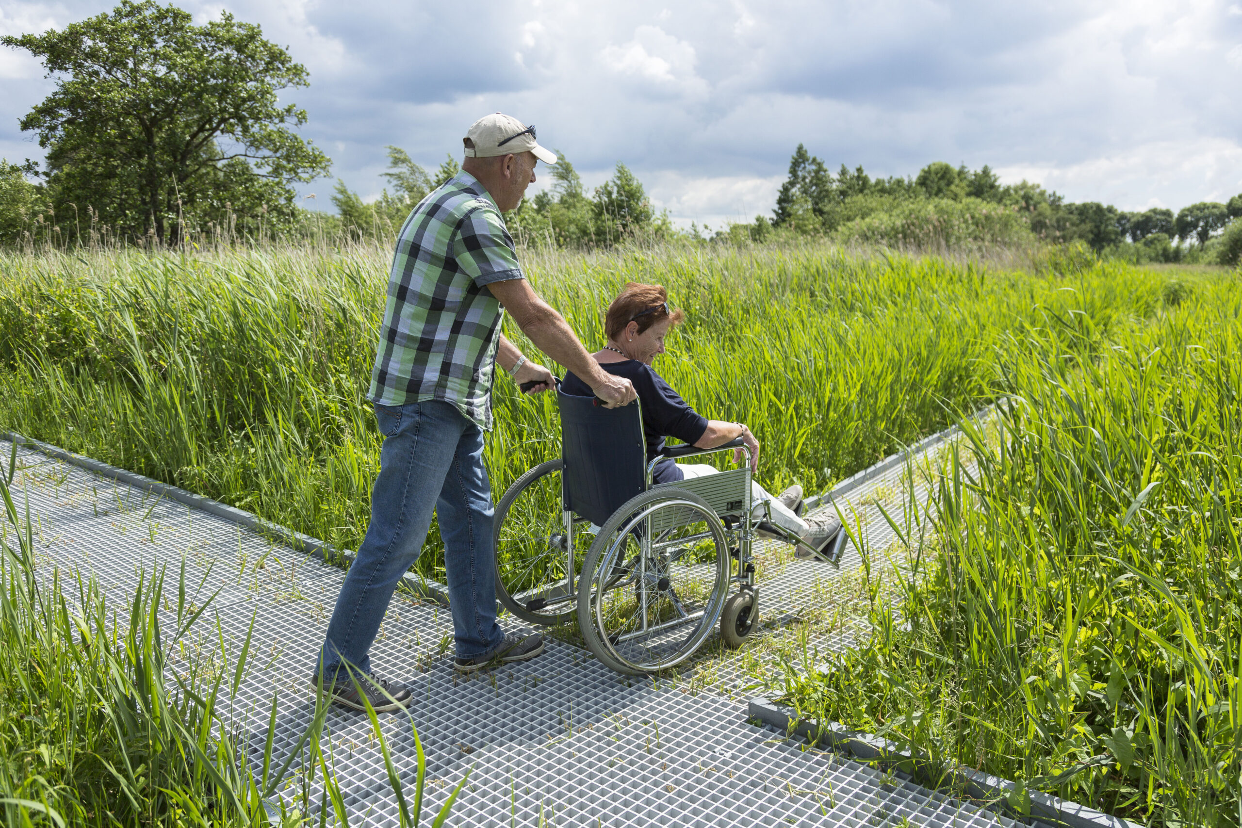 Een vrouw in een rolstoel gaat samen met een man een natuurgebied in
