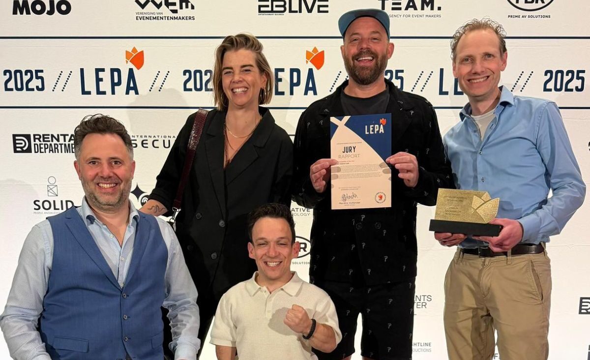 Vijf mensen poseren lachend met een LEPA-award en juryrapport voor een fotowand; één persoon zit in een rolstoel en één persoon is klein van stuk.