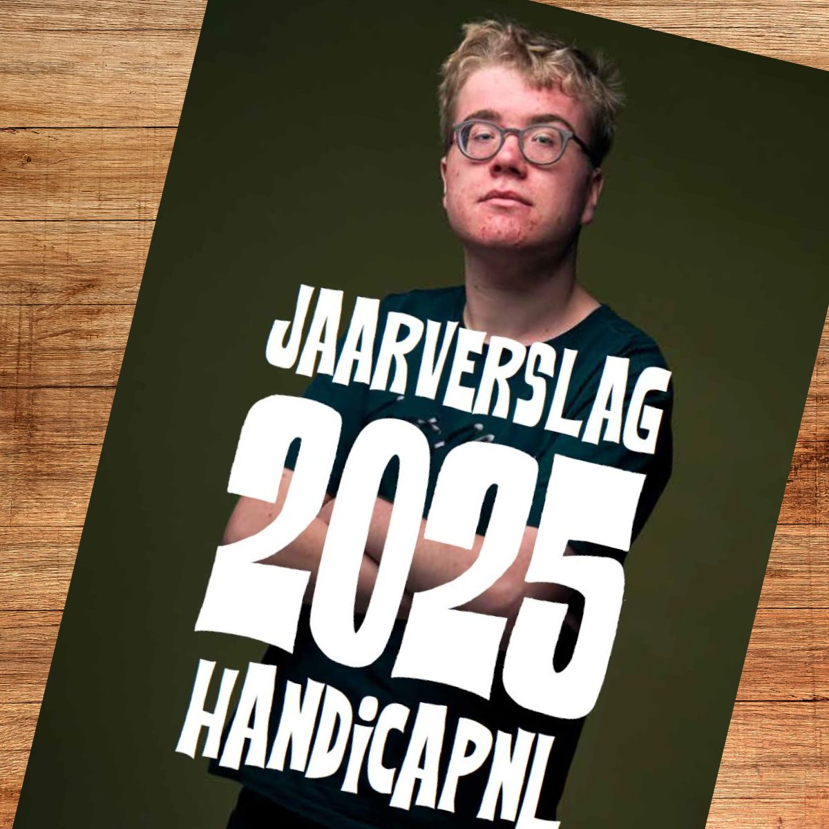 Omslag van het Jaarverslag 2025 van HandicapNL. Een portret van een jonge persoon met een bril en een zelfverzekerde blik vormt de achtergrond. In grote witte letters staat 'JAARVERSLAG 2025 HANDICAPNL'. De omslag ligt schuin op een houten ondergrond.